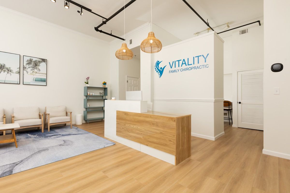 The Vitality Family Chiropractic reception desk, painted in white with wood accent, in front of a white wall