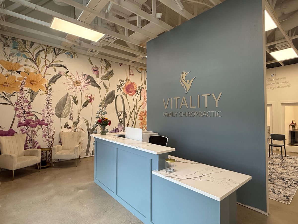The Vitality Family Chiropractic reception desk, painted dusty blue, in front of a colorful floral wall mural
